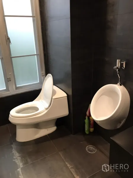 Detached House for rent in Wang Thonglang, Bangkok - Modern bathroom with dark tiles, toilet and wall-mounted urinal beside frosted window