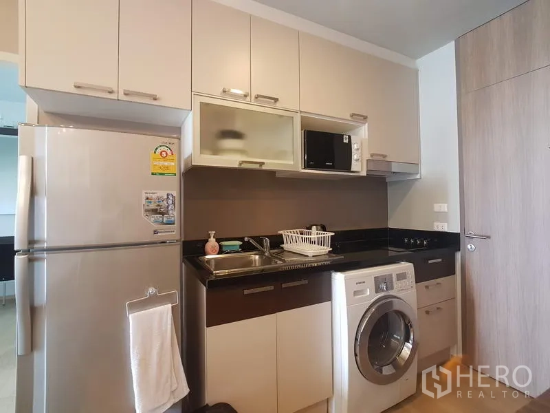 Condominium for rent in Bangkok - Compact modern kitchen with cabinets, granite countertop, refrigerator, microwave and washing machine.