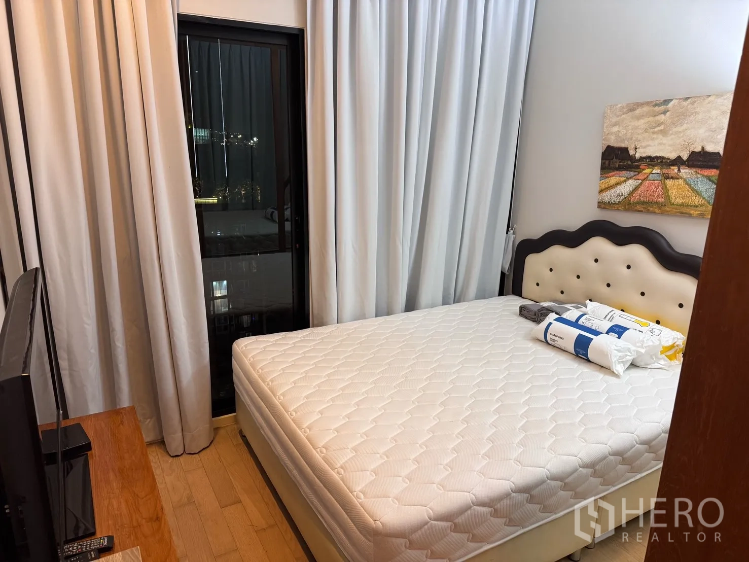 คอนโด for rent or sale in Watthana, Bangkok - ห้องนอนที่สองเตียงหัวเตียงบุผ้า ชั้นวางทีวี และประตูกระจกบานเลื่อนพร้อมผ้าม่าน เห็นเสี้ยววิวเมือง