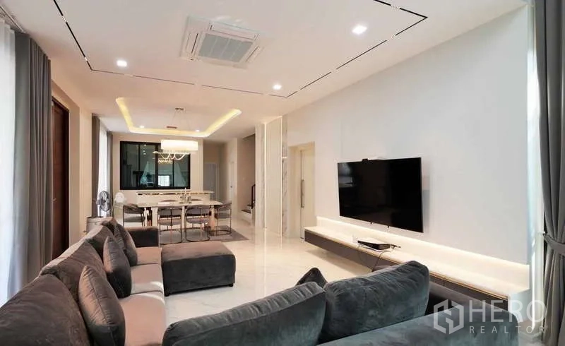 Detached House for rent or sale in Thanyaburi, Pathum Thani - Spacious lounge with sectional sofa, cassette ceiling air-conditioner and TV feature wall.