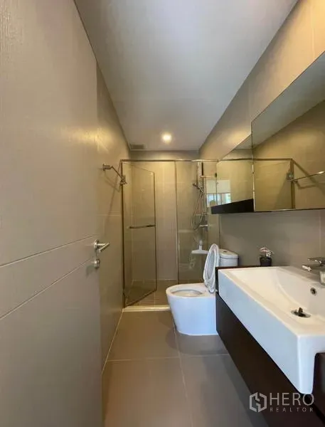 Townhouse for rent in Yan Nawa, Bangkok - Contemporary bathroom featuring a glass-enclosed shower, long mirror, and wall-hung vanity.