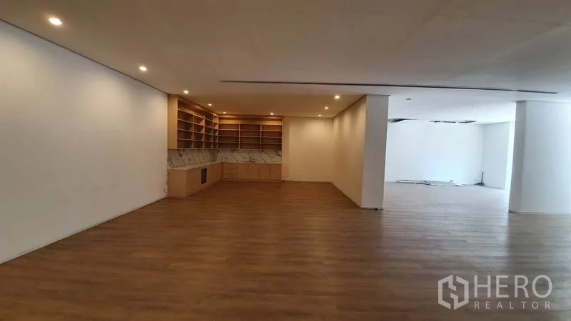 零售空间 出租在Khlong Toei, Bangkok - 宽阔展厅区域，带展示架区与中央立柱，暖色LED灯。