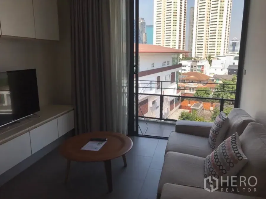 Condominium for rent in Watthana, Bangkok - Bright living room with sofa and TV opening to a balcony with city views in an Ekkamai condo.