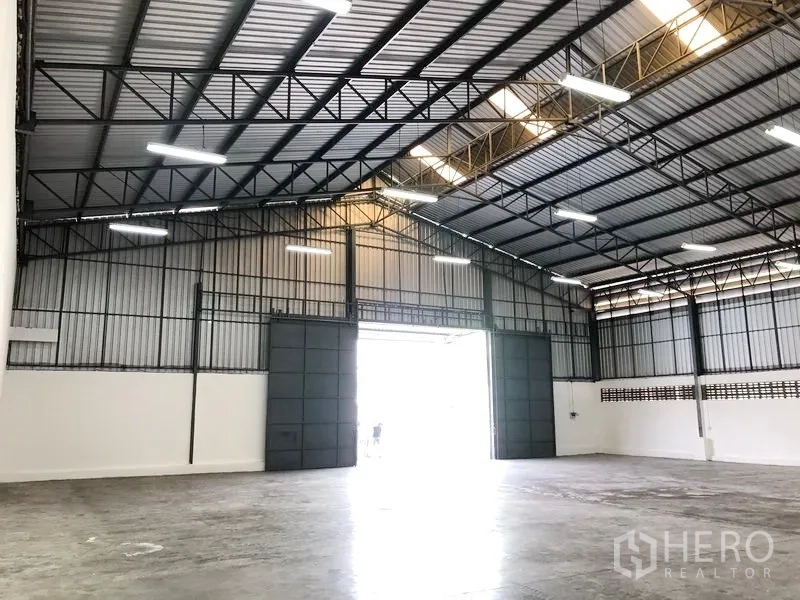 Warehouse for rent in Pak Kret, Nonthaburi - Interior facing the main doors featuring high-clearance steel structure and a large opening for truck access.