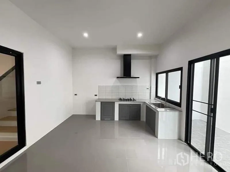Townhouse for sale in Watthana, Bangkok - Minimalist kitchen with gas hob, range hood, sink and large windows.