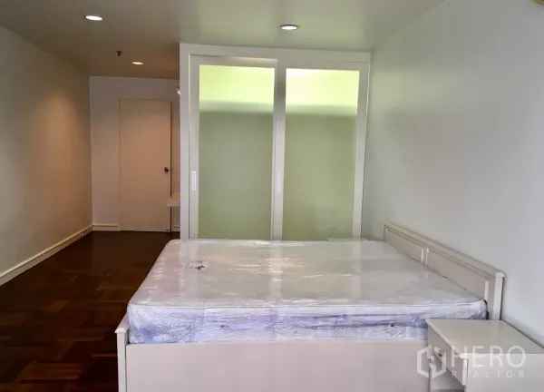 Condominium for rent or sale in Watthana, Bangkok - Bright master bedroom with parquet floors, white bed and frosted‑glass wardrobe in a Watthana, Bangkok condo.