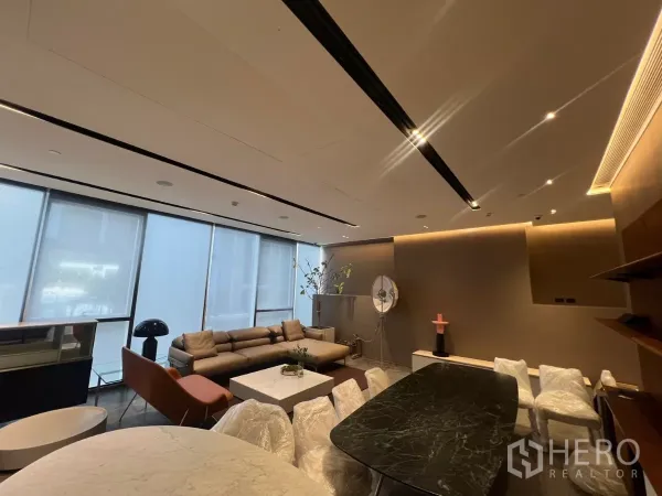 พื้นที่ขายปลีก ให้เช่า - มุมมองกว้างของพื้นที่ มีโซฟาตัวยาว ม่านม้วน ผ้าเพดานซ่อนแสง และโต๊ะหินเข้มบนพื้นกระเบื้อง.