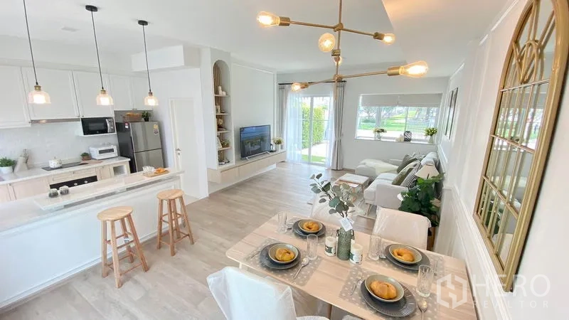 联排别墅 出租在Prawet, Bangkok - 从餐桌望向客厅，中岛厨房、电视背景墙与落地窗