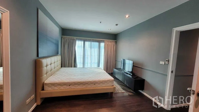 คอนโด ให้เช่าในKhlong Toei, Bangkok - ห้องนอนมาสเตอร์มองไปยังประตูกระจกระเบียง ตู้ทีวี และไฟดาวน์ไลท์เหนือพื้นไม้เข้ม