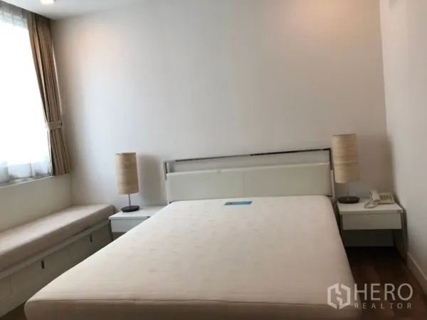 คอนโด ให้เช่าในPathum Wan, Bangkok - ห้องนอนบรรยากาศสงบ เตียงคู่ โต๊ะข้างพร้อมโคมไฟ และที่นั่งริมหน้าต่างมีที่เก็บของ