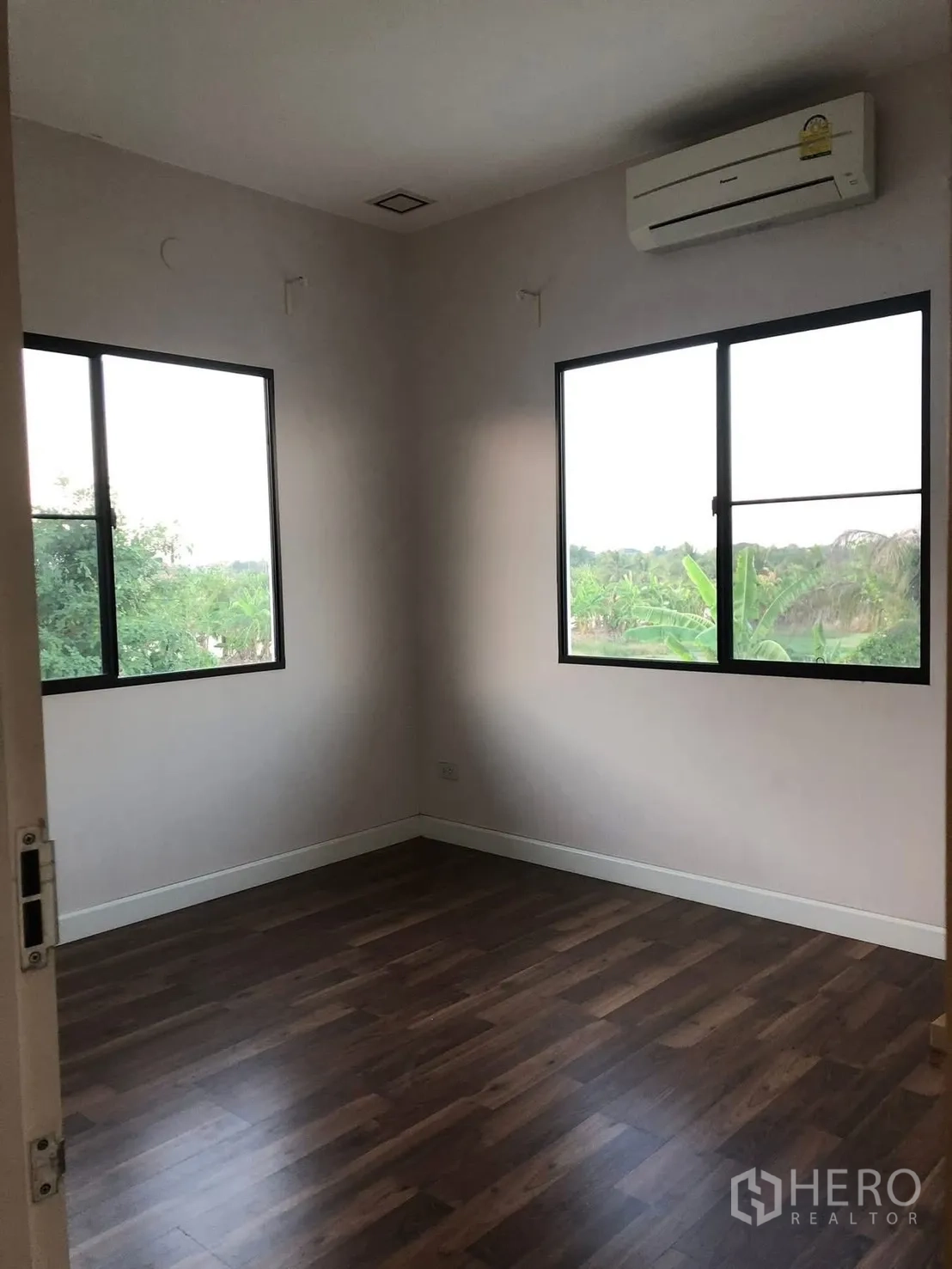 บ้านเดี่ยว for rent in Prawet, Bangkok - ห้องนอนมุมบ้านพื้นไม้ มีหน้าต่างสองบานและเครื่องปรับอากาศ เห็นวิวต้นไม้