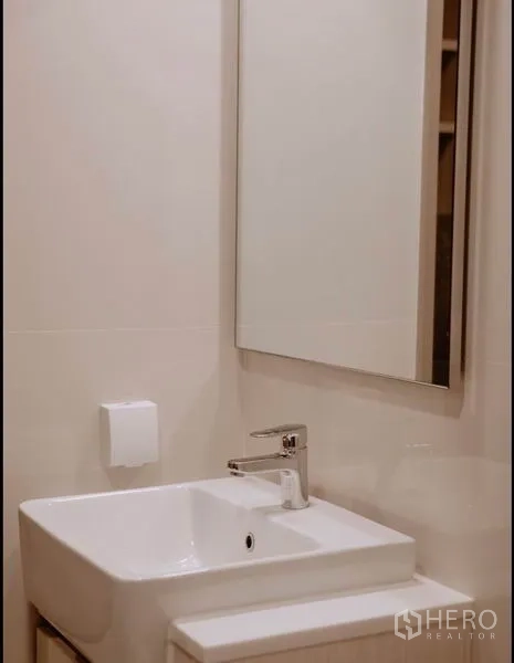 Condominium for sale in Chatuchak, Bangkok - Close-up of white basin and mirror in a minimalist bathroom.