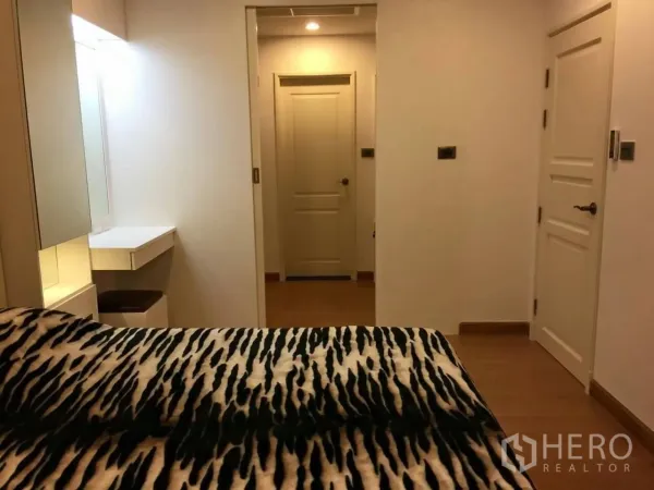 Condominium for sale in Huai Khwang, Bangkok - Bedroom view toward the hallway with sliding door, built-in vanity and warm wood flooring.