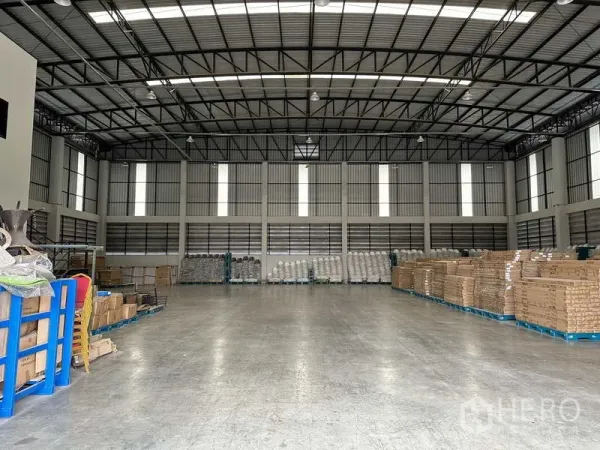 货栈 出租在Bang Phli, Samut Prakan - 仓库内部空间宽敞，钢结构高屋顶与天窗，抛光混凝土地面，堆放托盘货物。