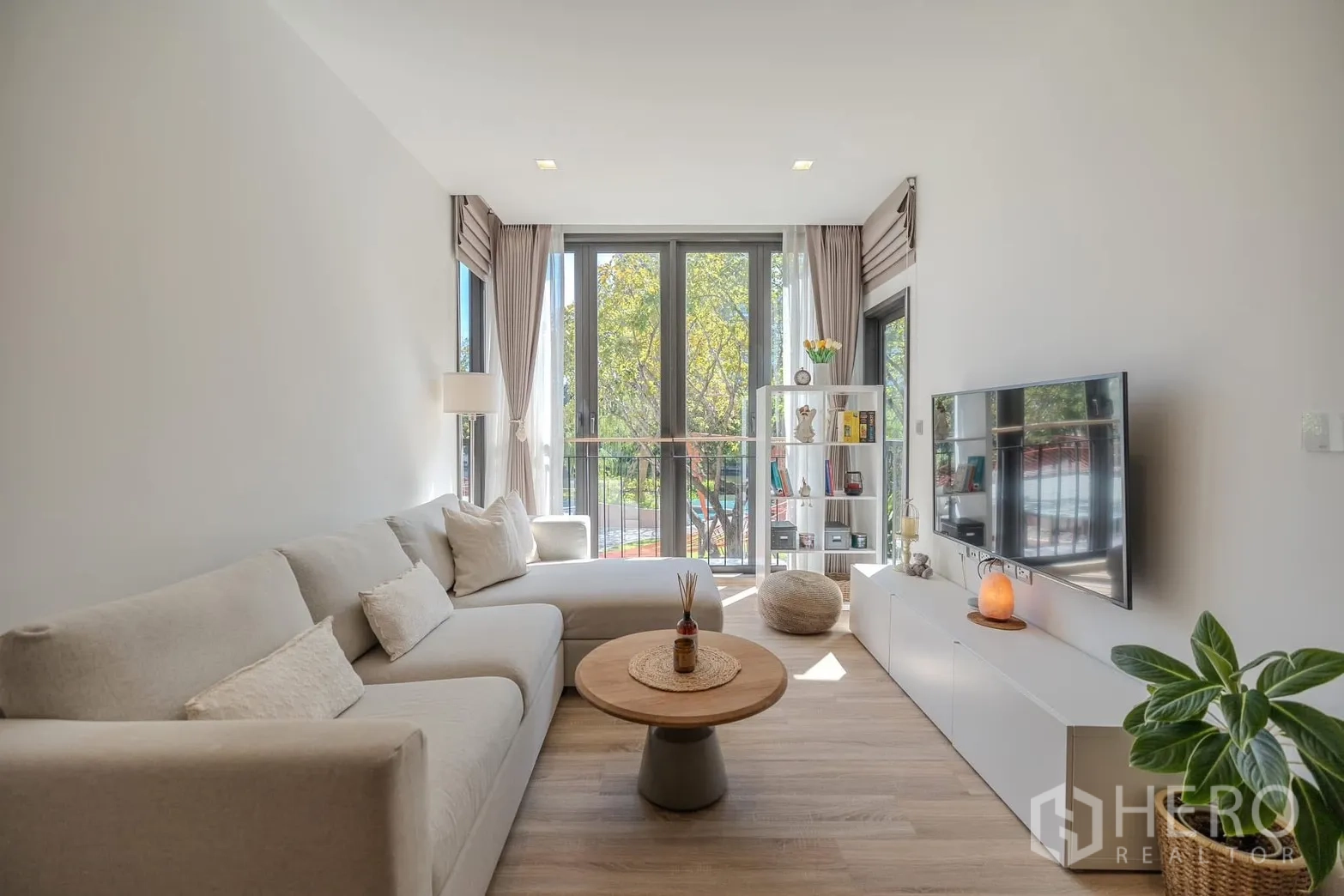 Condominium for rent in Watthana, Bangkok - Sunlit living area with sectional sofa, large windows and a display shelf.