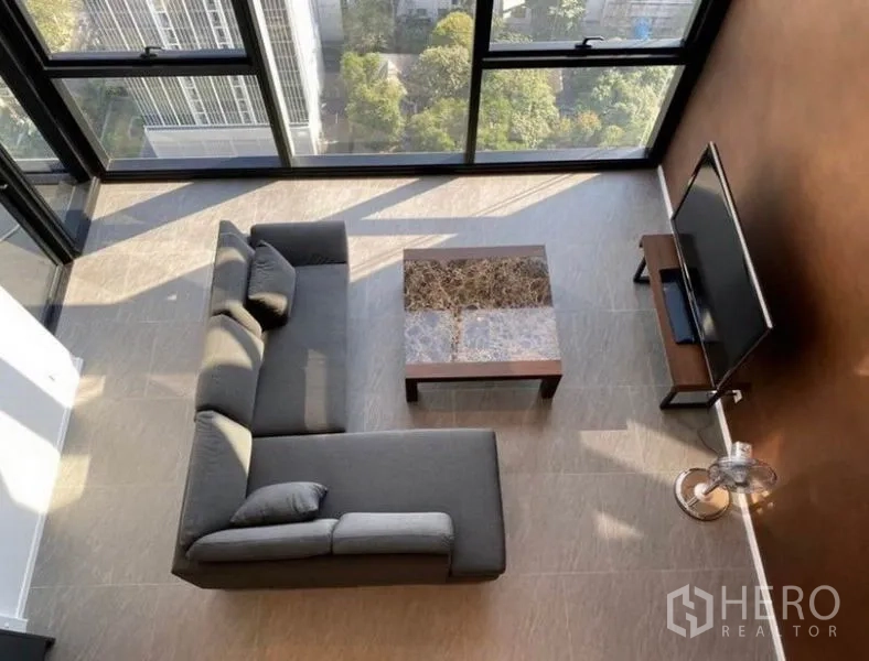 公寓 出租在Bang Rak, Bangkok - 从上方看起居区，L形沙发靠近双层高玻璃窗，眺望绿意景观。