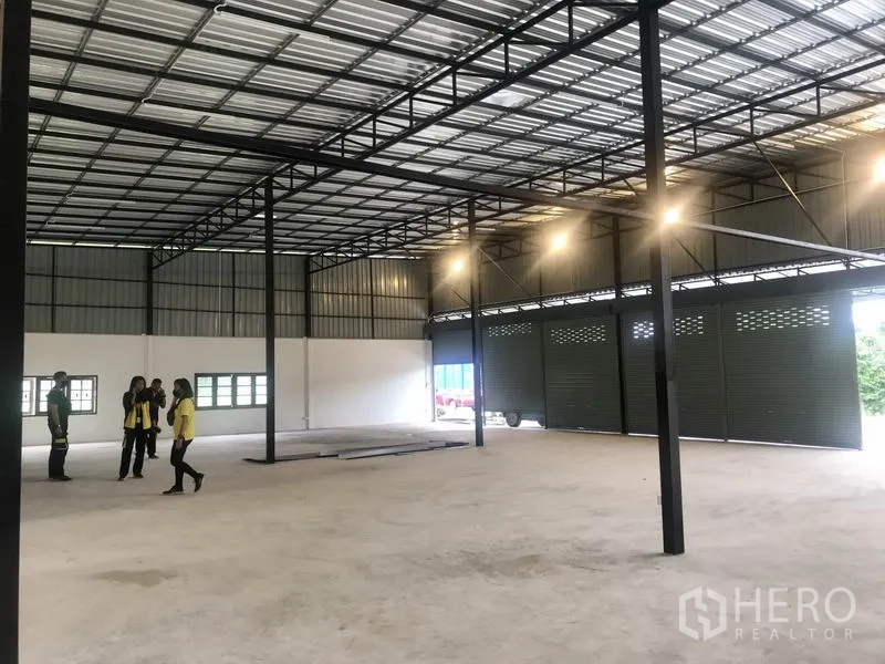 Warehouse for rent in Pathum Thani - Clear-span warehouse interior with high steel roof, concrete floor, and roller shutter bays.