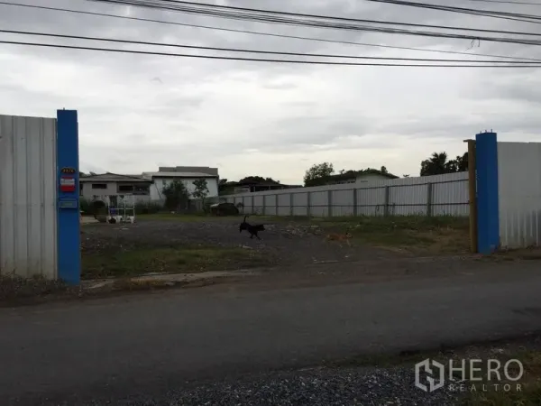 Warehouse for rent in Mueang Pathum Thani, Pathum Thani - Street-facing double gate leading into an expansive fenced compound with ample yard space.
