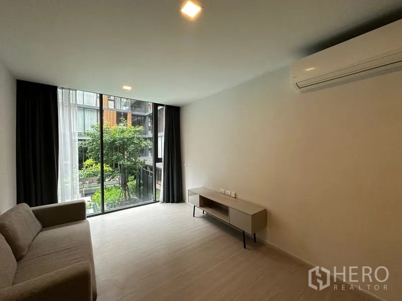 คอนโด ให้เช่าในKhlong Toei, Bangkok - ห้องนั่งเล่นสไตล์มินิมอล มีโซฟา ชั้นวางทีวี แอร์ และประตูกระจกบานเลื่อนมองเห็นสวนและสระ