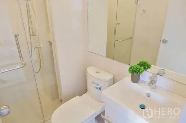 Condominium for rent in Huai Khwang, Bangkok - Bright bathroom with glass-enclosed shower, vanity sink, and toilet in a Huai Khwang condo.