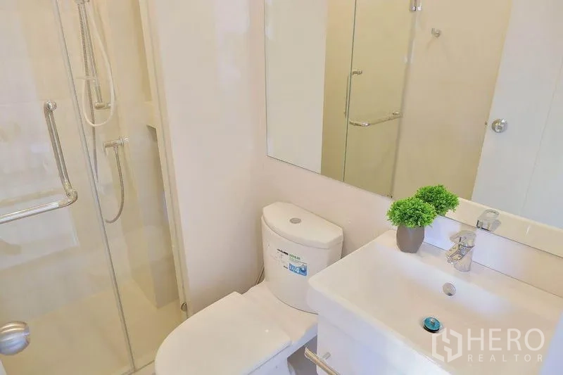 Condominium for rent in Huai Khwang, Bangkok - Bright bathroom with glass-enclosed shower, vanity sink, and toilet in a Huai Khwang condo.