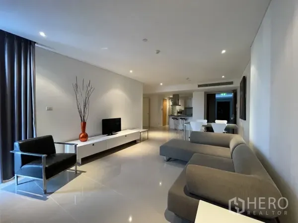 คอนโด ให้เช่าหรือขายในWatthana, Bangkok - ห้องนั่งเล่นแบบโอเพ่นแพลน โซฟาเข้ามุมสีเทา ชุดวางทีวี เก้าอี้หนัง และม่านสูงจรดเพดานต่อเนื่องไปยังครัว.