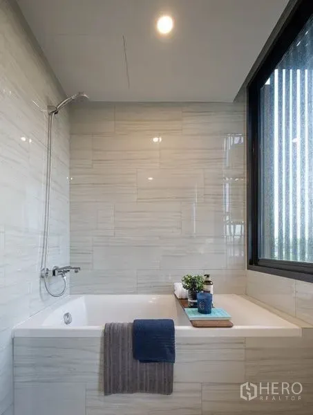 Condominium for rent or sale in Watthana, Bangkok - Bathroom with white tiled walls, a soaking tub with shower and a window for natural light.