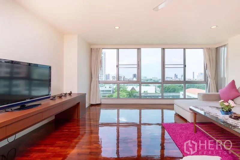 Condominium for rent in Bang Rak, Bangkok - Bright family room with panoramic windows, L-shaped sofa, TV console and city and green views.