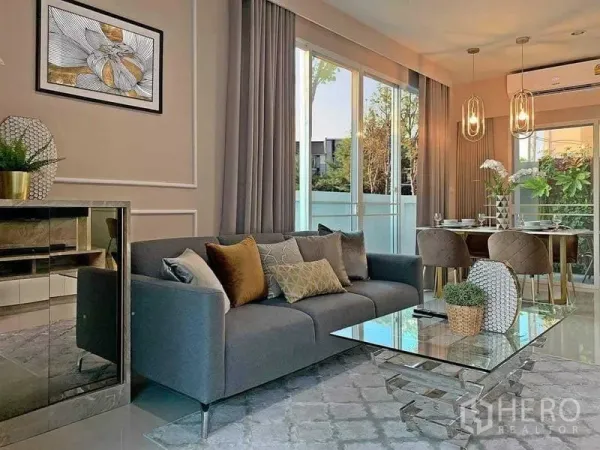 联排别墅 出售在Mueang Nonthaburi, Nonthaburi - 采光充足的客厅，灰色沙发和玻璃茶几，推拉门通向露台