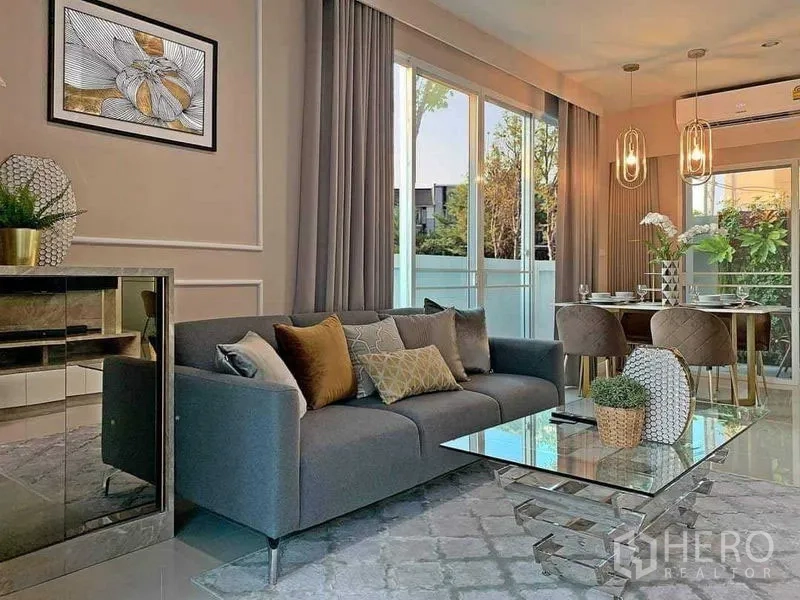 联排别墅 出售在Mueang Nonthaburi, Nonthaburi - 采光充足的客厅，灰色沙发和玻璃茶几，推拉门通向露台