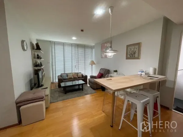 คอนโด ขายในKhlong Toei, Bangkok - ห้องนั่งเล่นสว่างแบบเปิดโล่ง มีชุดโซฟา ชั้นวางทีวี และเคาน์เตอร์บาร์ ข้างหน้าต่างบานเกล็ดสูงจรดเพดาน