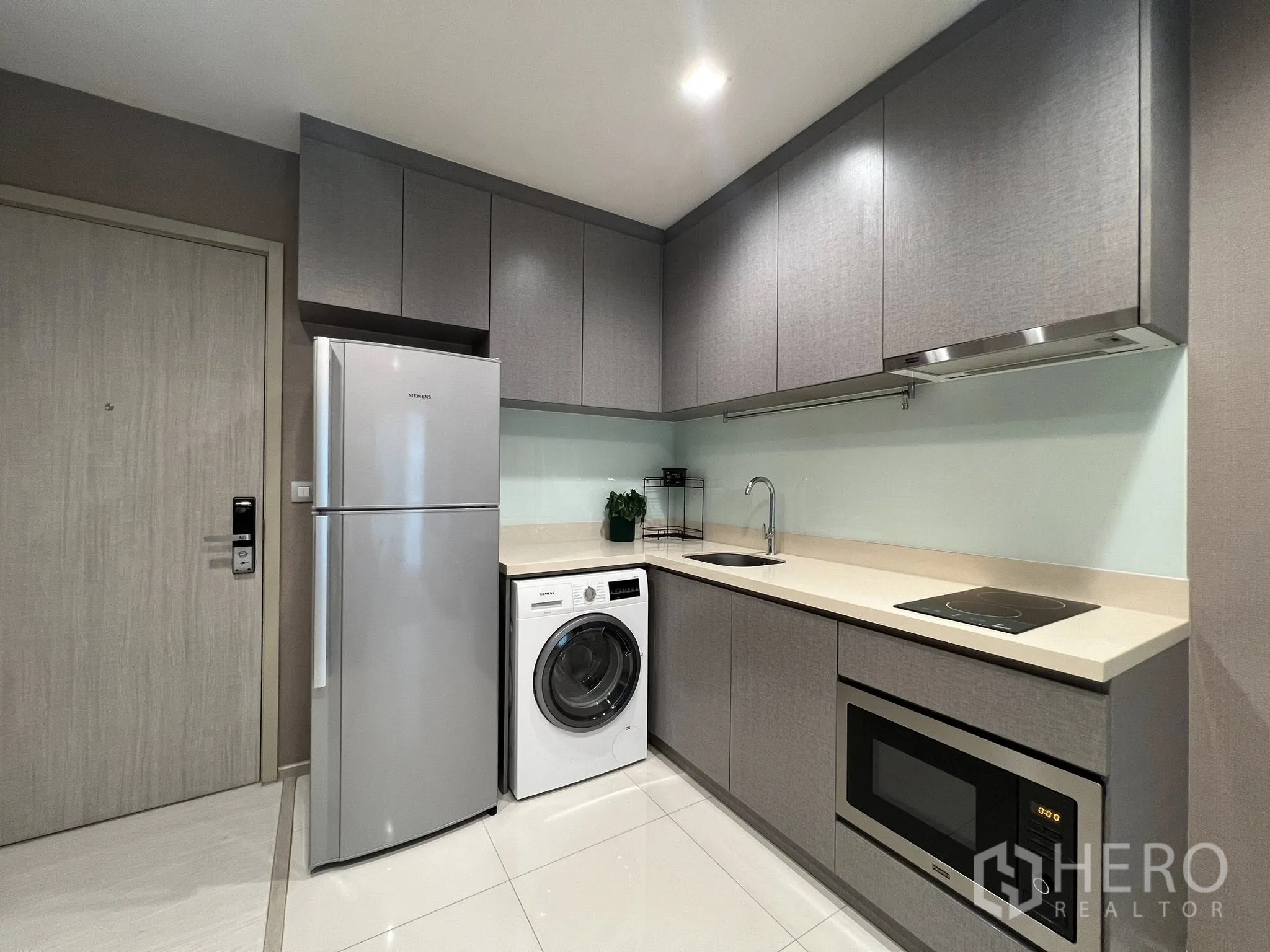 Condominium for rent in Khlong Toei, Bangkok - Full kitchen view showing overhead cabinets, microwave, glass backsplash, and appliances.