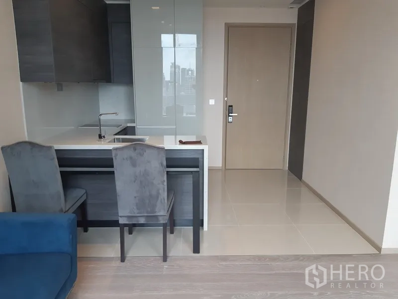 คอนโด ให้เช่าหรือขายในWatthana, Bangkok - ครัวเปิดขนาดกะทัดรัดพร้อมไอส์แลนด์ท็อปหินและเก้าอี้ทานอาหารใกล้ประตูทางเข้า