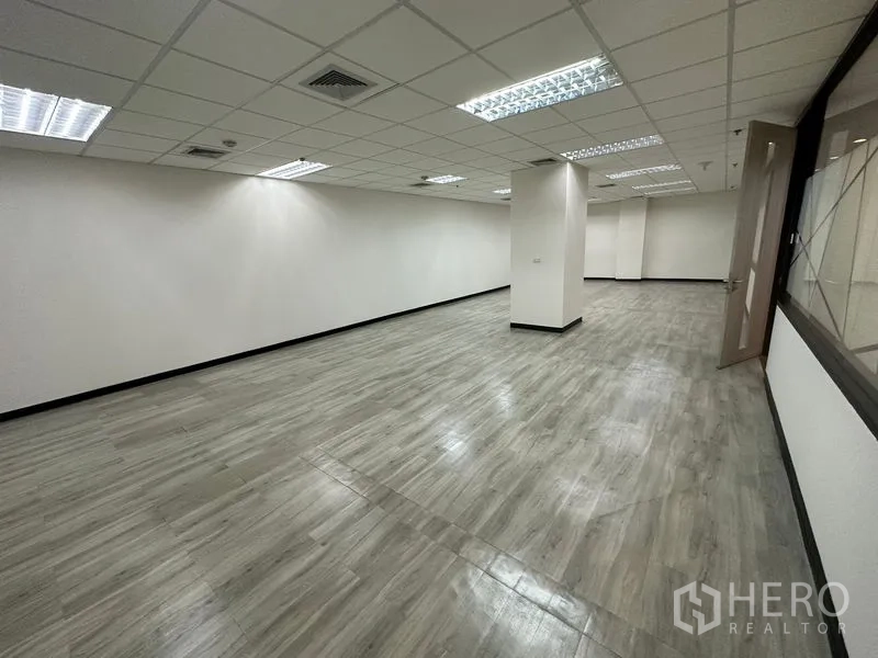 Office Space for rent - Large open-plan office with drop ceiling lights, white walls, columns and grey vinyl flooring.