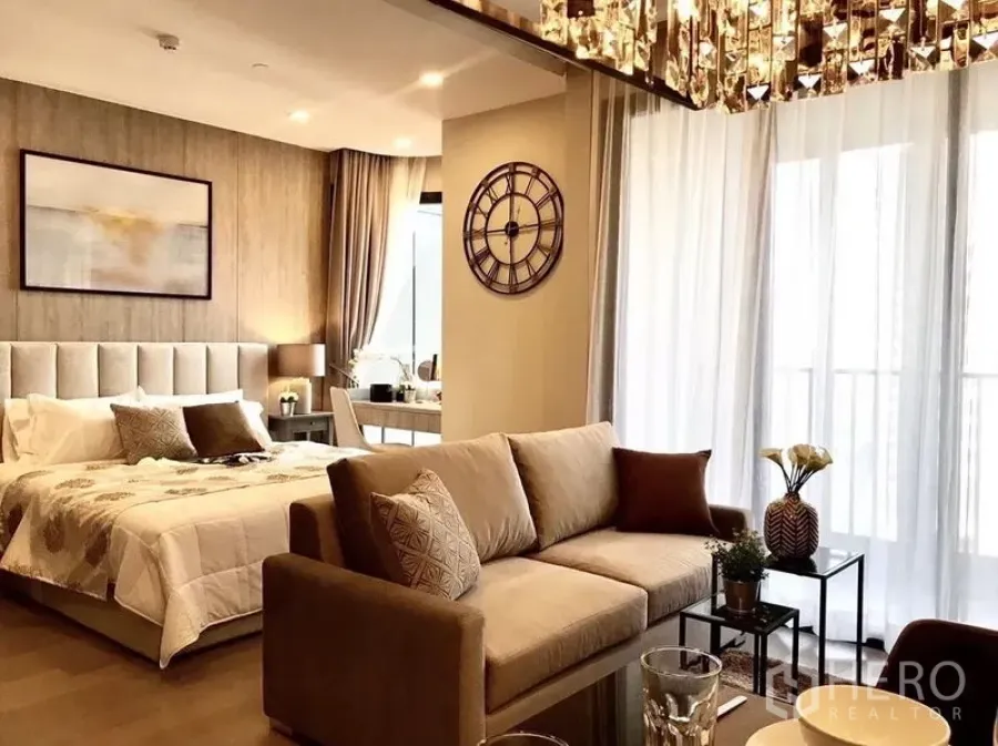 Condominium for rent in Watthana, Bangkok - Open-plan living and bedroom with sofa, upholstered bed, large windows and sheer curtains.