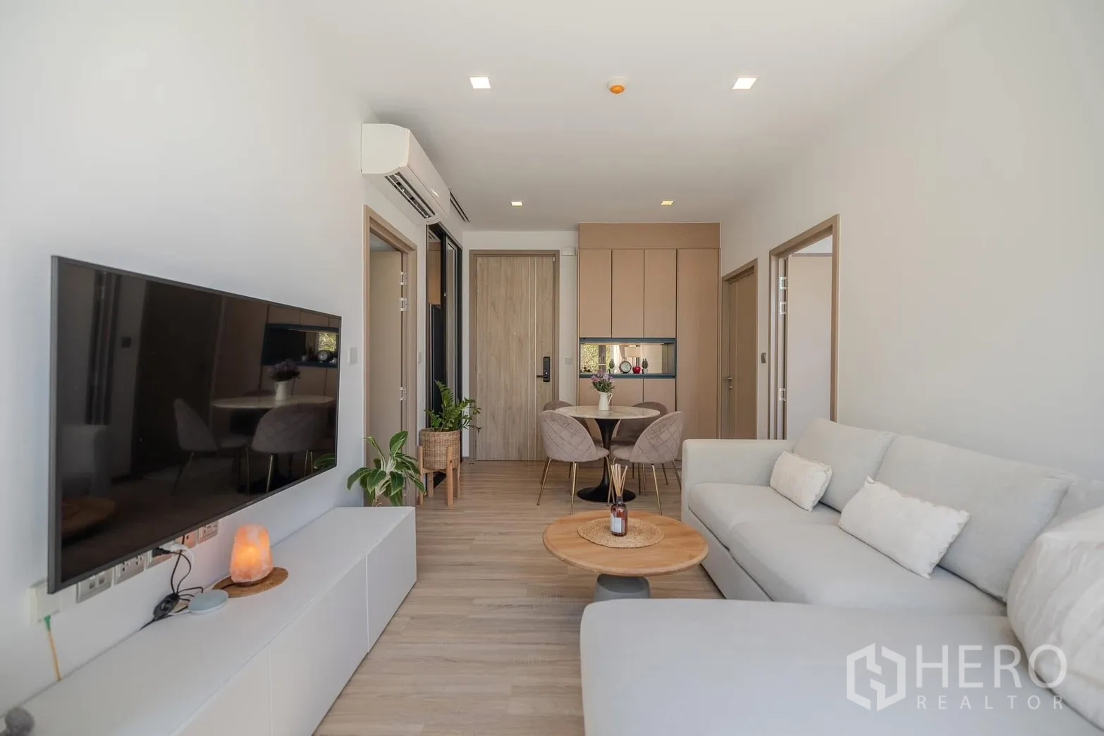Condominium for rent in Watthana, Bangkok - Living room with wall-mounted TV, light sofa and wood flooring.