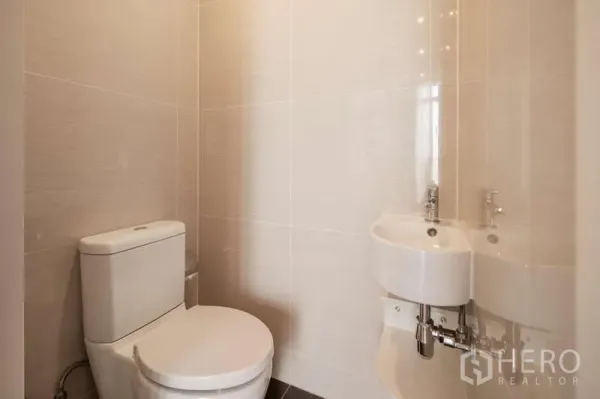 Condominium for rent in Khlong Toei, Bangkok - Clean guest toilet with white ceramic fixtures and tiled walls.