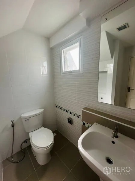 Detached House for sale in Prawet, Bangkok - Bright bathroom with small window, sink, toilet and decorative tile band.