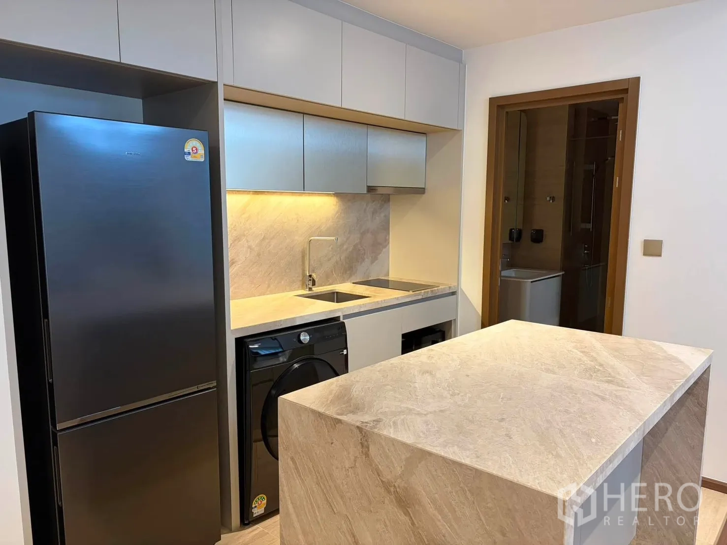 Condominium for rent in Watthana, Bangkok - Compact kitchen with stone island, sink, under-cabinet lighting, refrigerator, and washer.