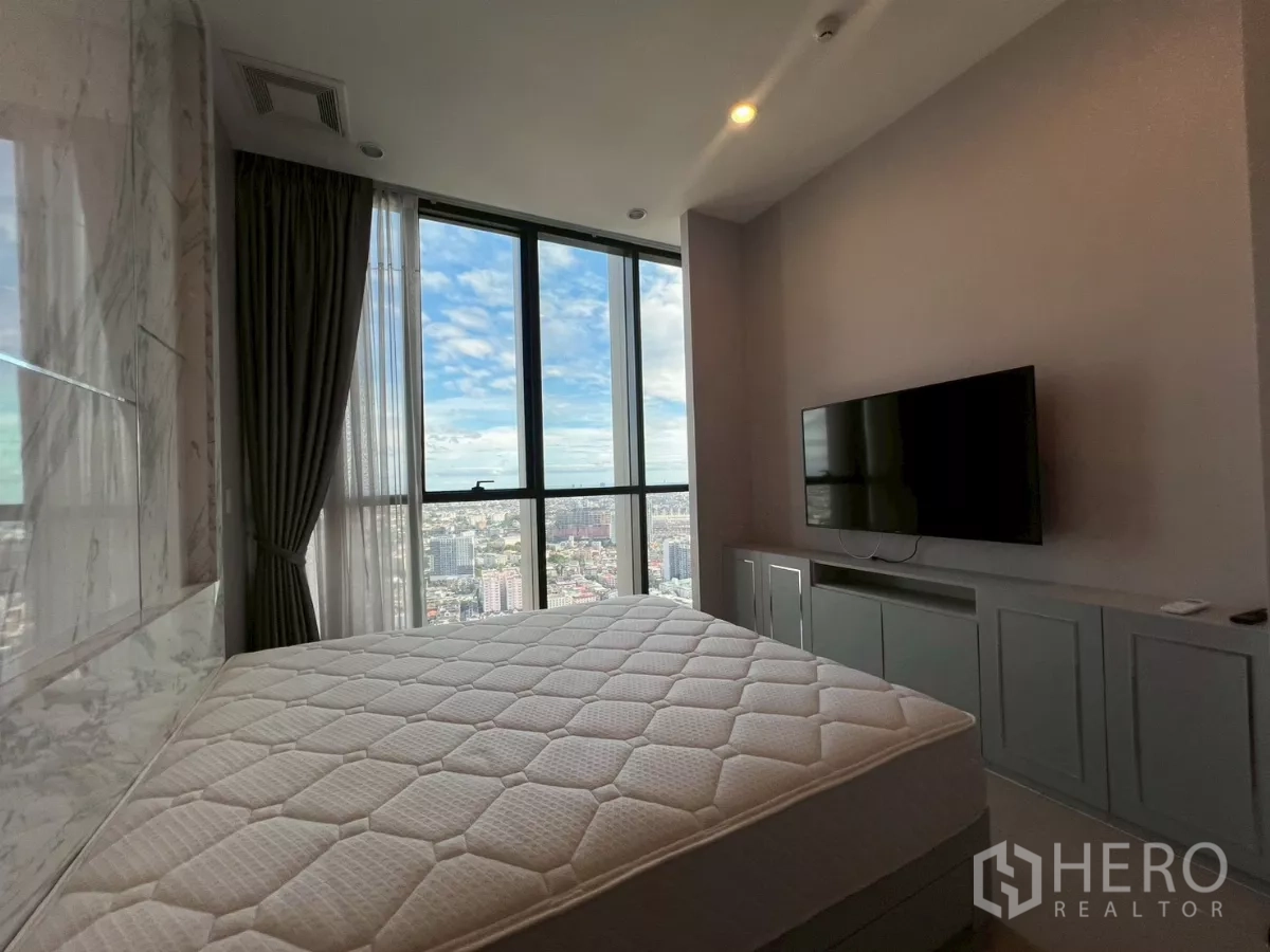Condominium for rent in Phra Khanong, Bangkok - Bedroom corner with mattress, TV cabinet, and wraparound floor-to-ceiling windows overlooking Bangkok.
