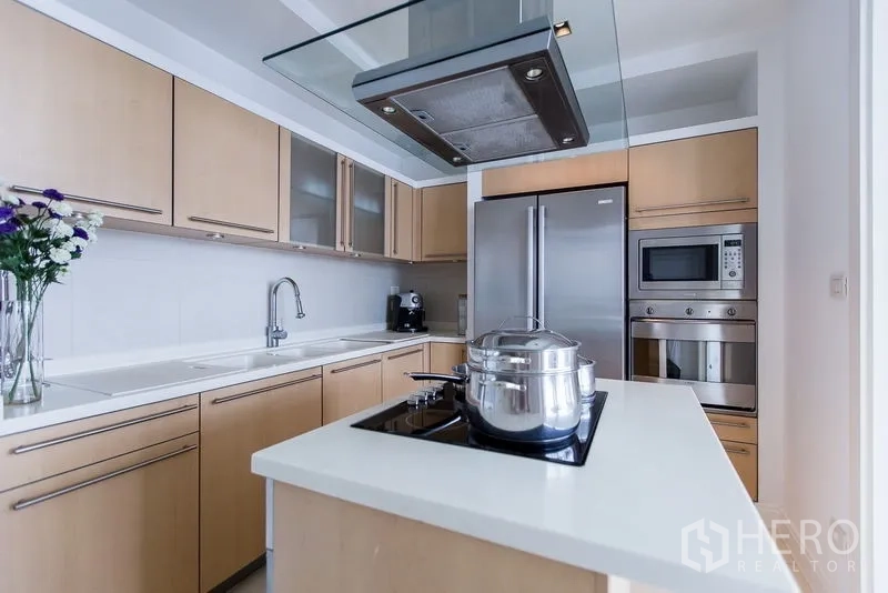 Condominium for rent in Pathum Wan, Bangkok - Modern kitchen with island cooktop, stainless appliances, and light wood cabinetry.