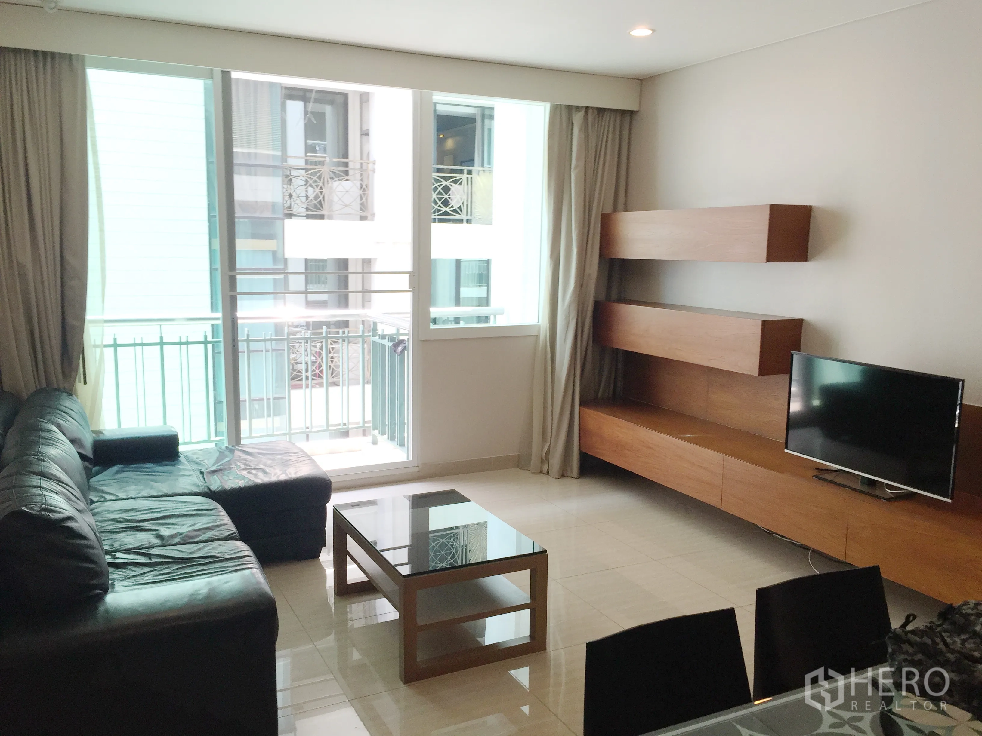 คอนโด ให้เช่าหรือขายในWatthana, Bangkok - ห้องนั่งเล่นสว่างเชื่อมระเบียง โซฟาหนัง ทีวี และชั้นไม้บิลท์อิน