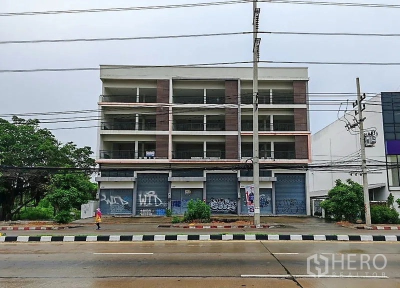 Home Office for rent or sale in Lam Luk Ka, Pathum Thani - Front elevation of the commercial building facing a main road with multiple shopfronts.