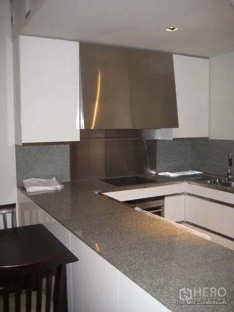 Condominium for rent or sale in Sathon, Bangkok - Modern U-shaped kitchen with granite countertop, white cabinets, stainless backsplash and a built-in hob.
