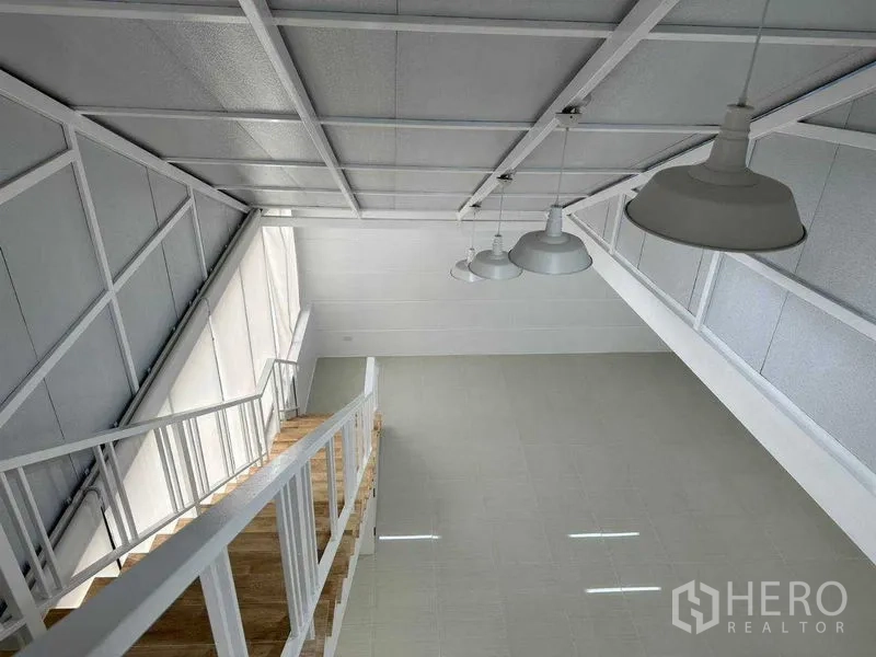 Office Space for rent or sale in Khlong Toei, Bangkok - View from the mezzanine showing pendant lights, sloped ceiling and a windowed wall.