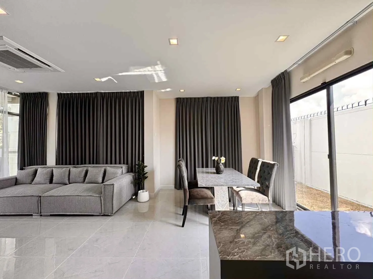 Detached House for rent in Bang Phli, Samut Prakan - Living-dining space with grey sofa, dining set and sliding glass door to the yard.