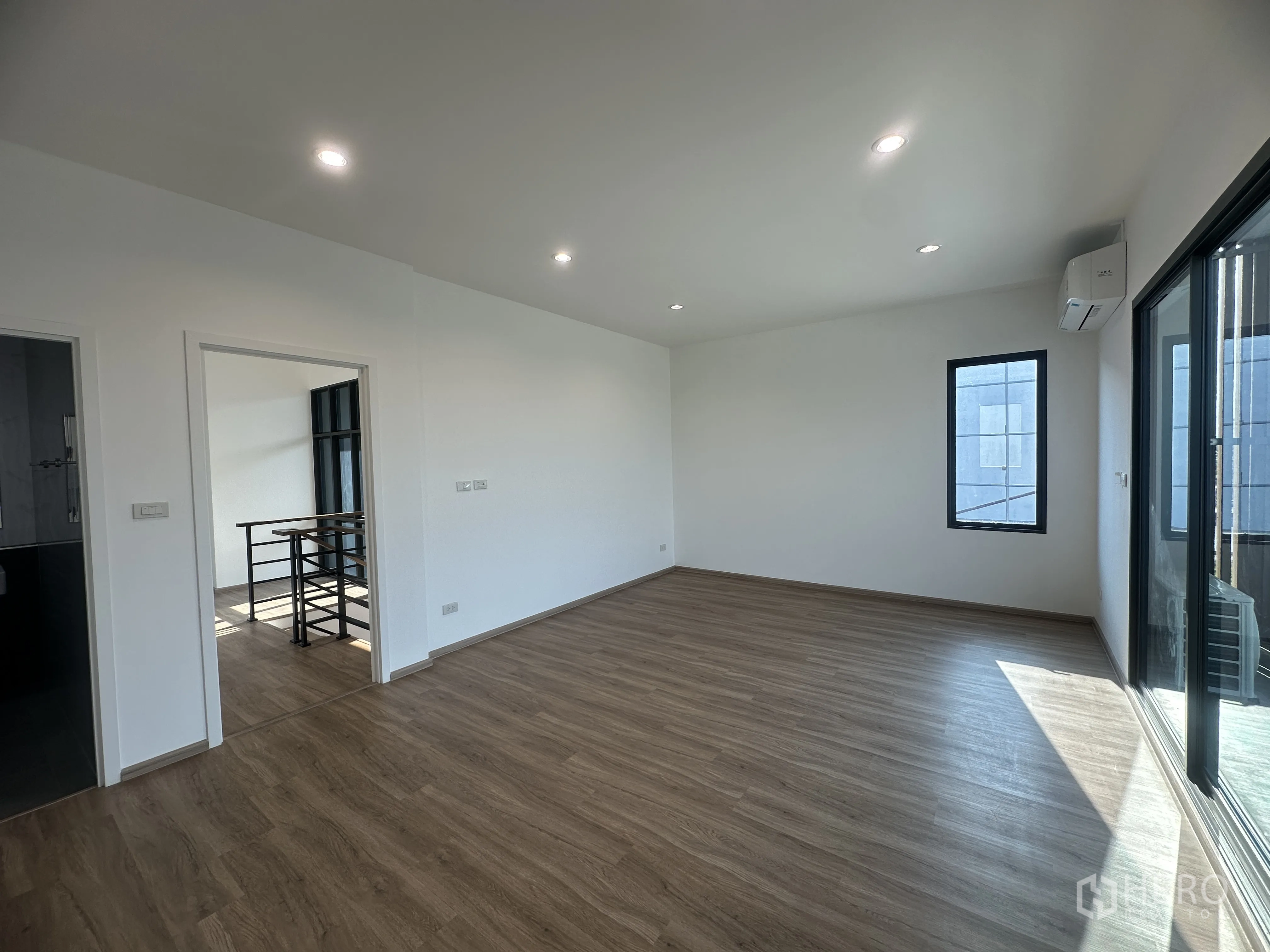 Home Office for sale in Khlong Luang, Pathum Thani - Upper-floor room with wood flooring, recessed lights, air conditioner, and sliding glass door to a balcony.