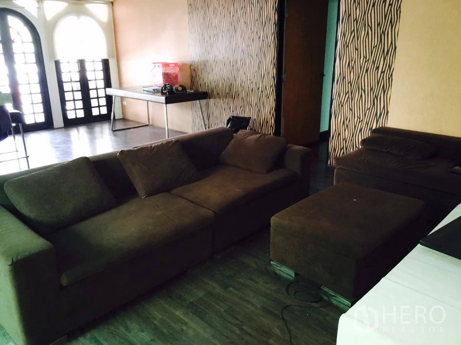 Detached House for rent in Wang Thonglang, Bangkok - Wang Thonglang detached house living room with brown sofas, ottoman, arched French doors and textured walls.