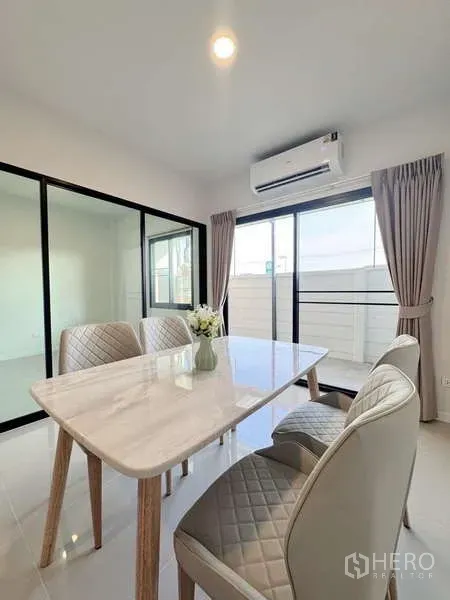 Townhouse for rent in Min Buri, Bangkok - Dining area with marble-top table, quilted chairs, air-conditioner and large sliding doors.