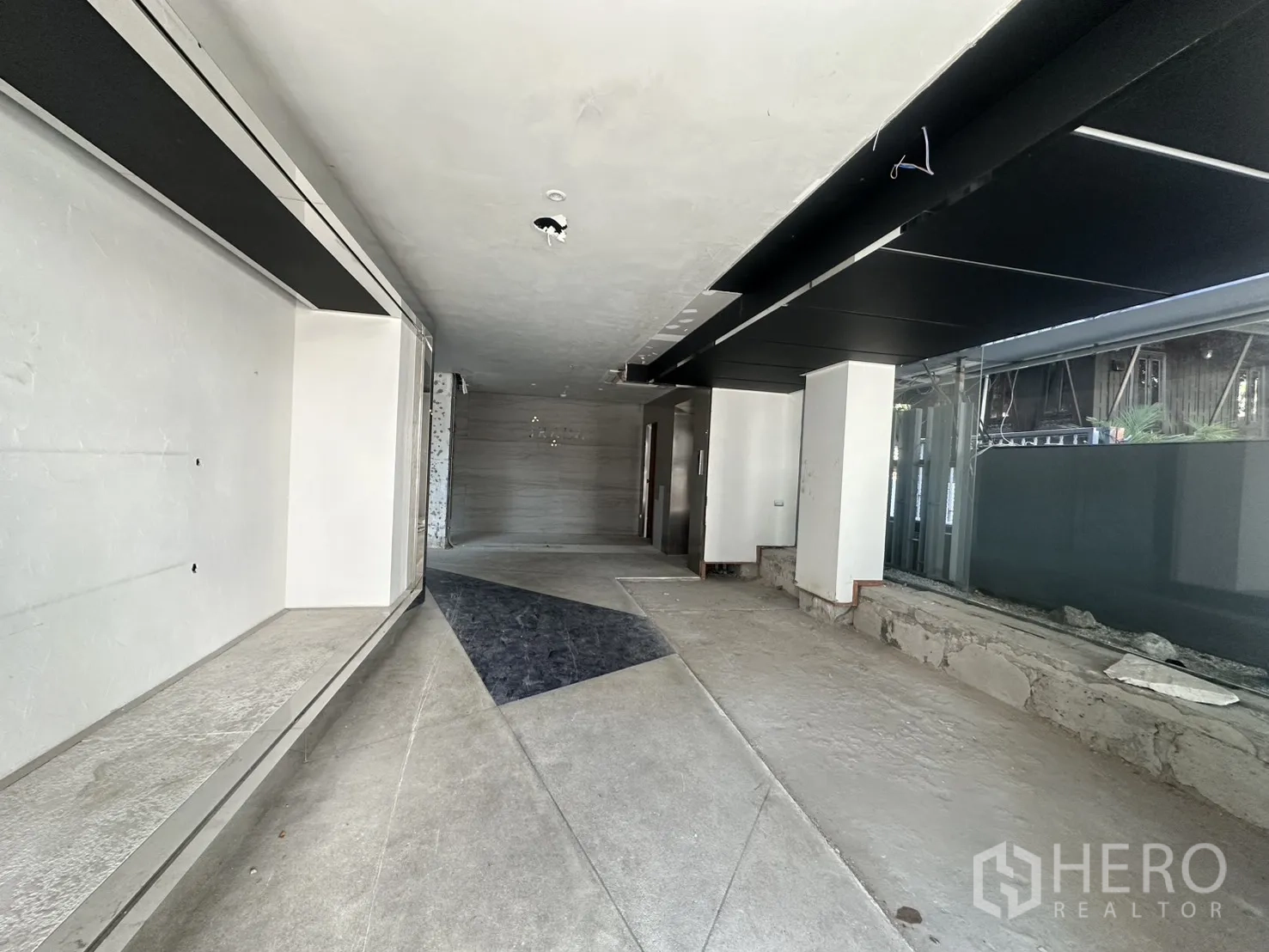 Retail Space for rent in Watthana, Bangkok - Long ground-floor retail interior under renovation with concrete floors, dark ceiling panels, and large side windows.